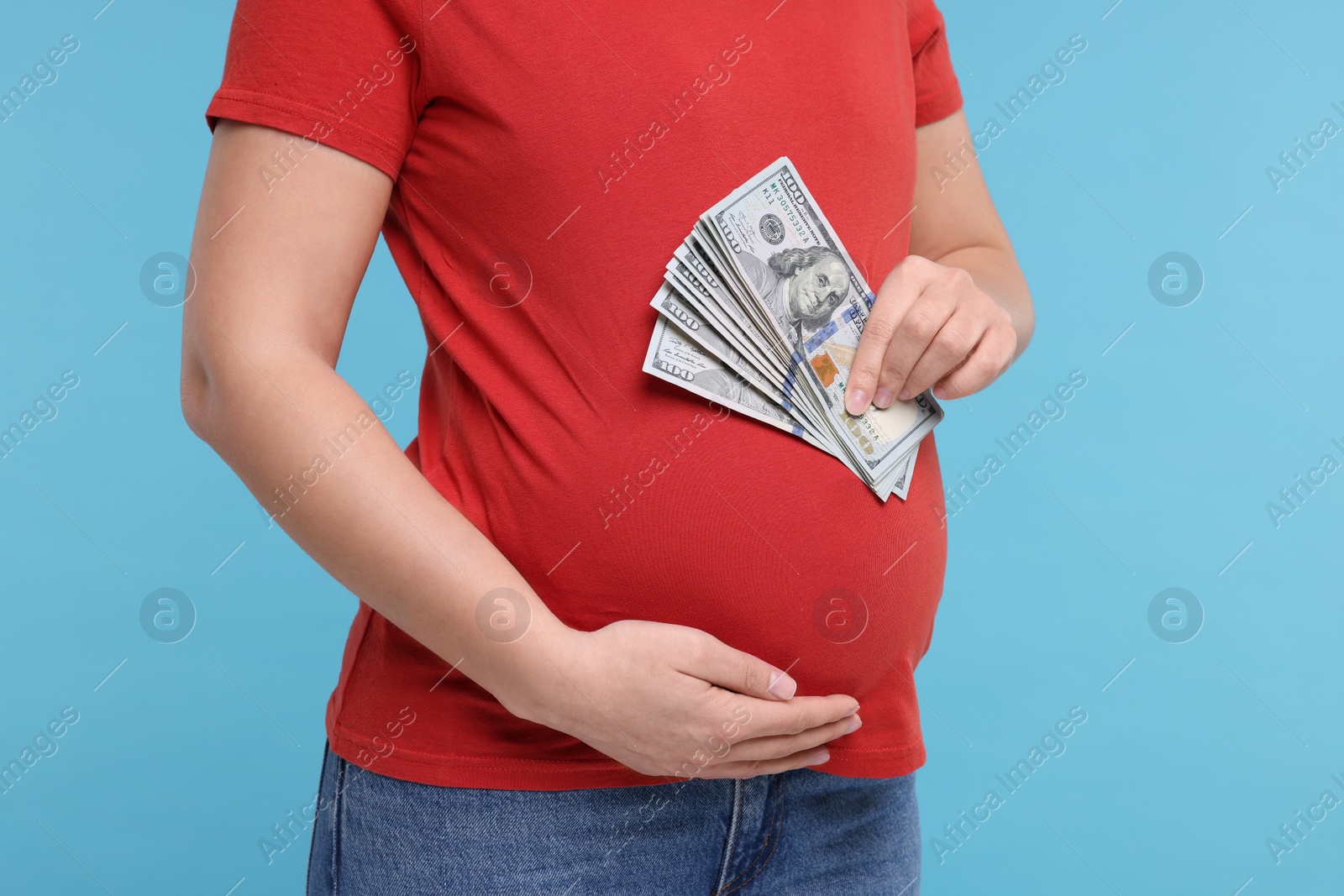 Photo of Surrogate mother. Pregnant woman with dollar banknotes on light blue background, closeup