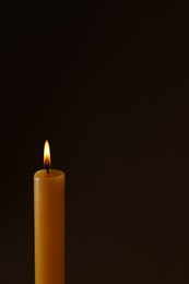 Photo of Burning church wax candle on dark background, space for text