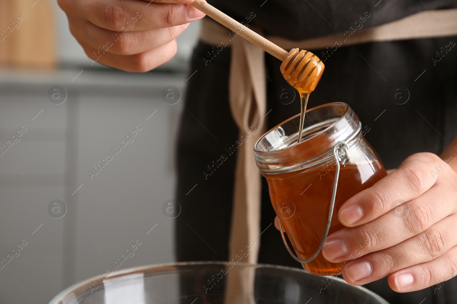 Photo of Woman with jar of honey and dipper in kitchen, closeup