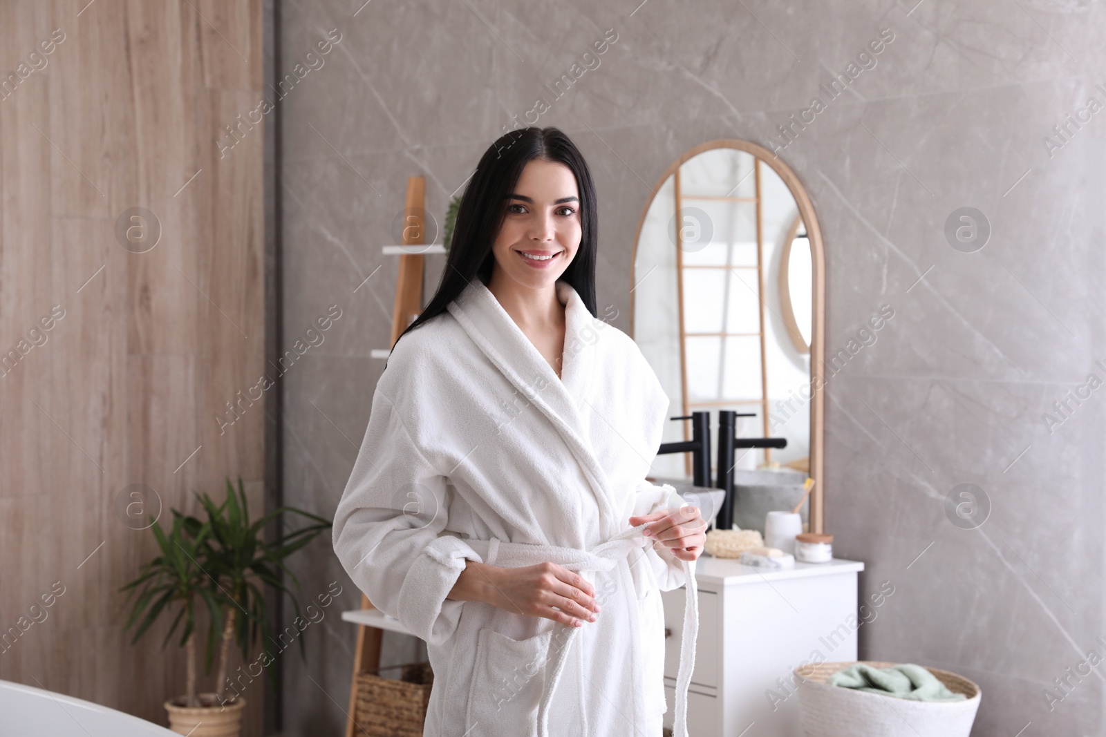 Photo of Beautiful young woman wearing soft white robe in bathroom