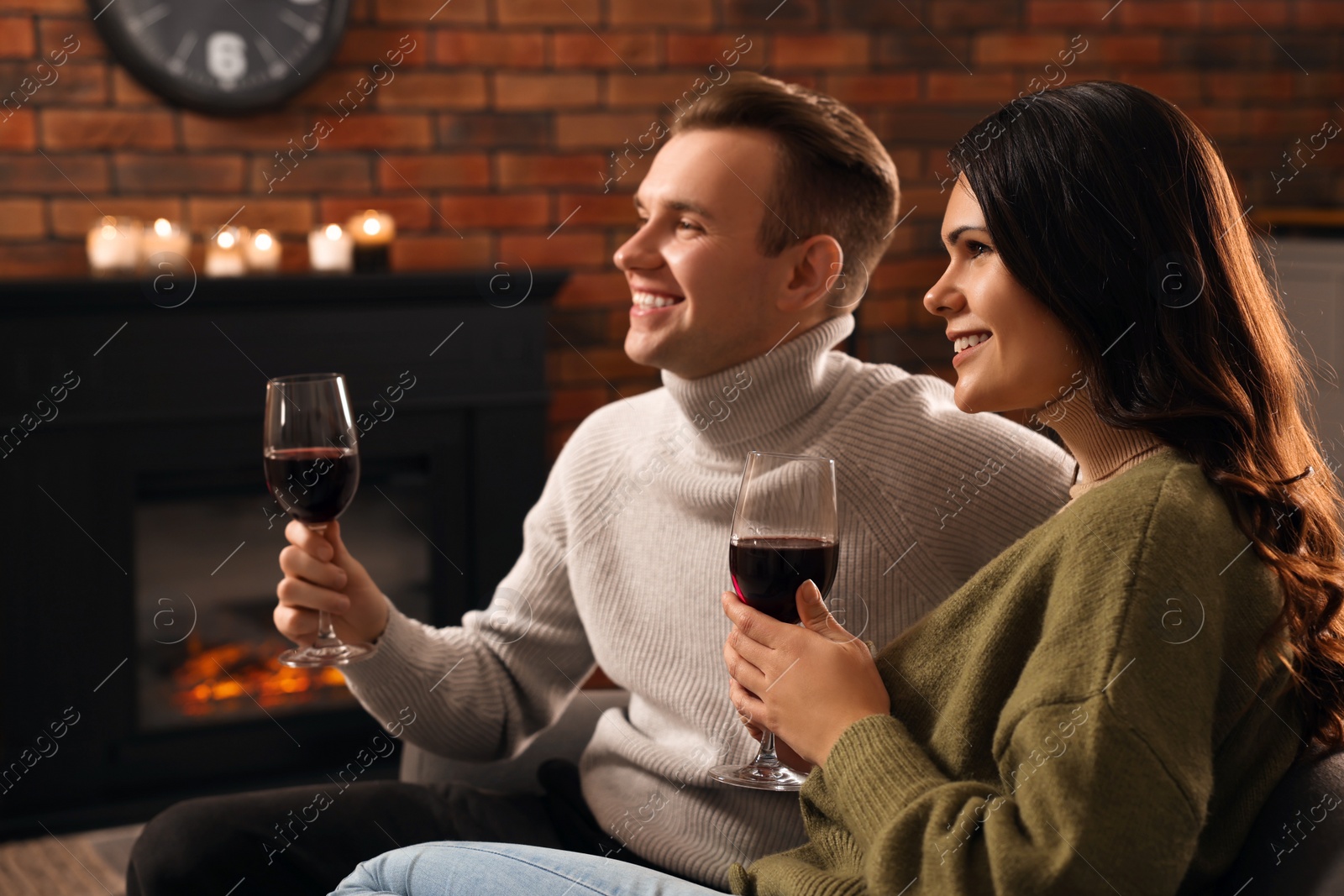 Photo of Happy lovely couple with glasses of wine resting together near fireplace at home