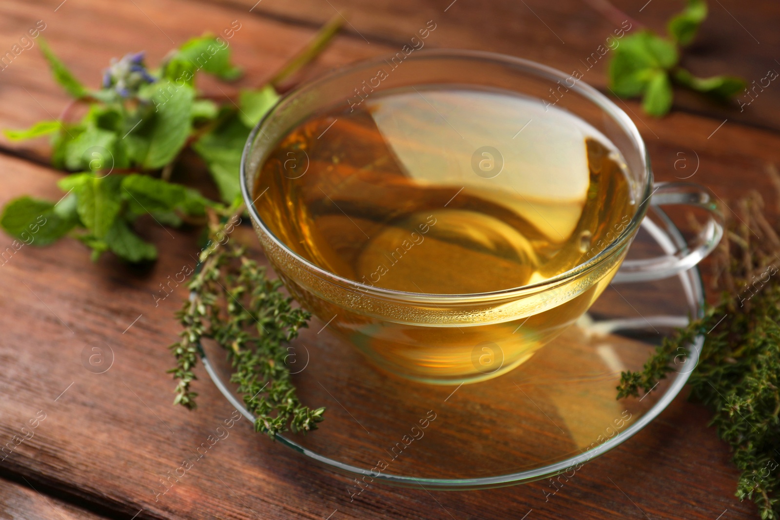 Photo of Cup of aromatic herbal tea and fresh thyme on wooden table, closeup