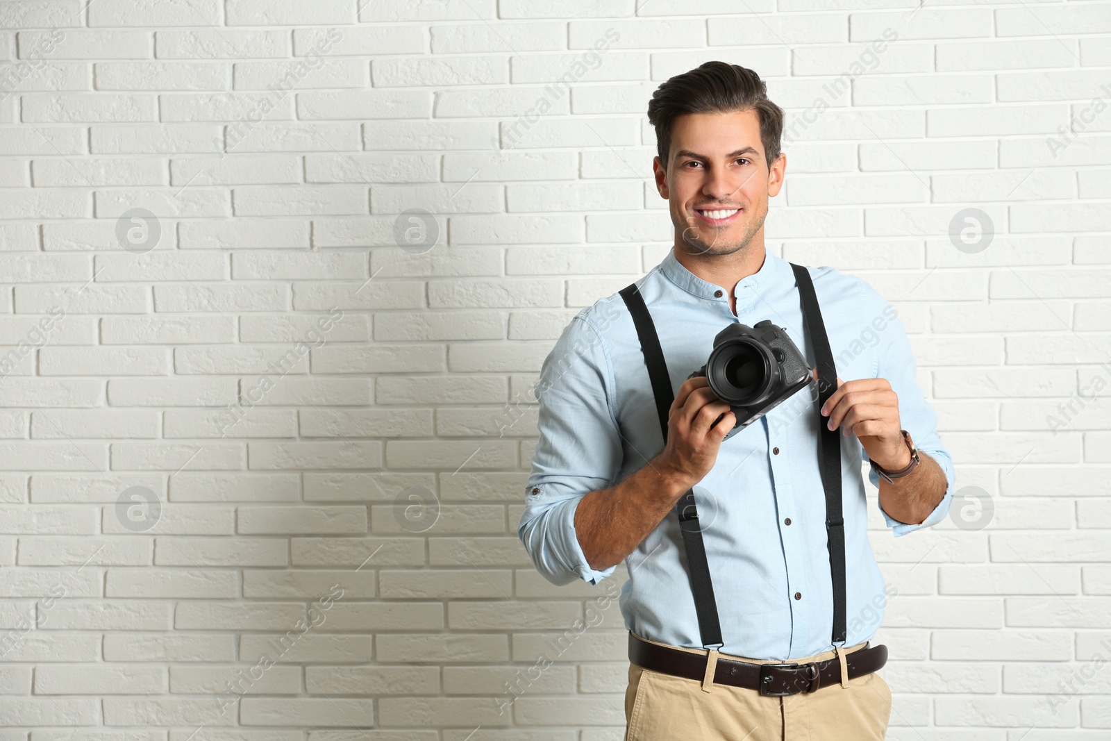 Photo of Professional photographer working near white brick wall in studio. Space for text