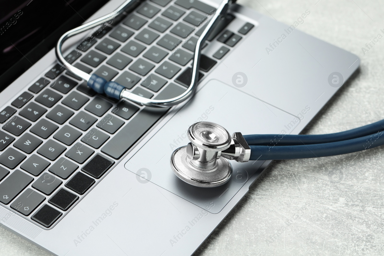 Photo of Stethoscope and modern laptop on grey table, closeup