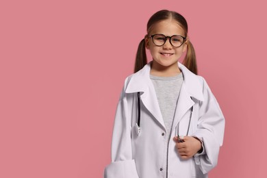 Photo of Little girl in medical uniform with stethoscope on pink background. Space for text