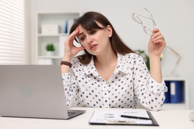 Overwhelmed woman sitting at table with laptop in office