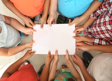 Photo of Little children holding sheet of paper in hands together, top view. Unity concept