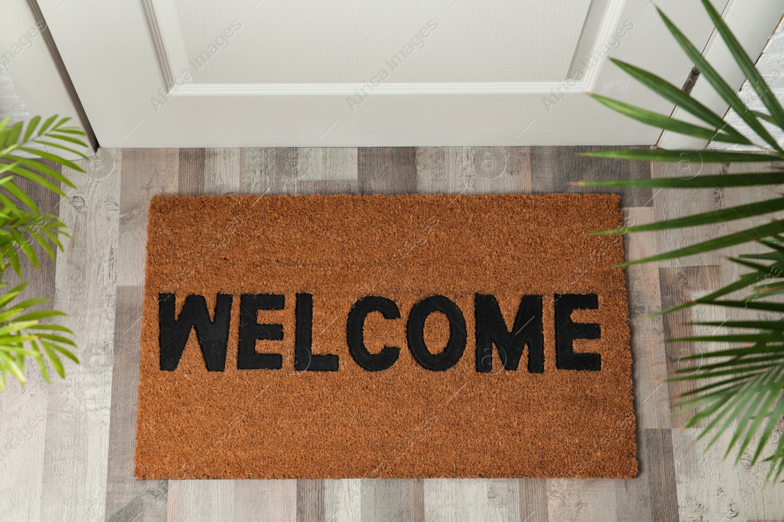 Photo of Door mat with word Welcome on wooden floor in hall, top view