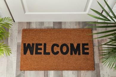 Photo of Door mat with word Welcome on wooden floor in hall, top view