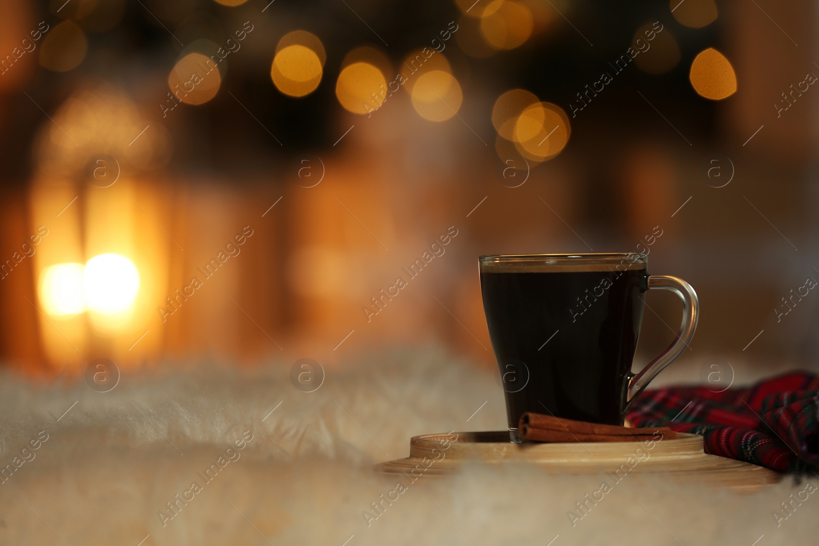 Photo of Cup of coffee on white fur against blurred lights, space for text. Cozy winter