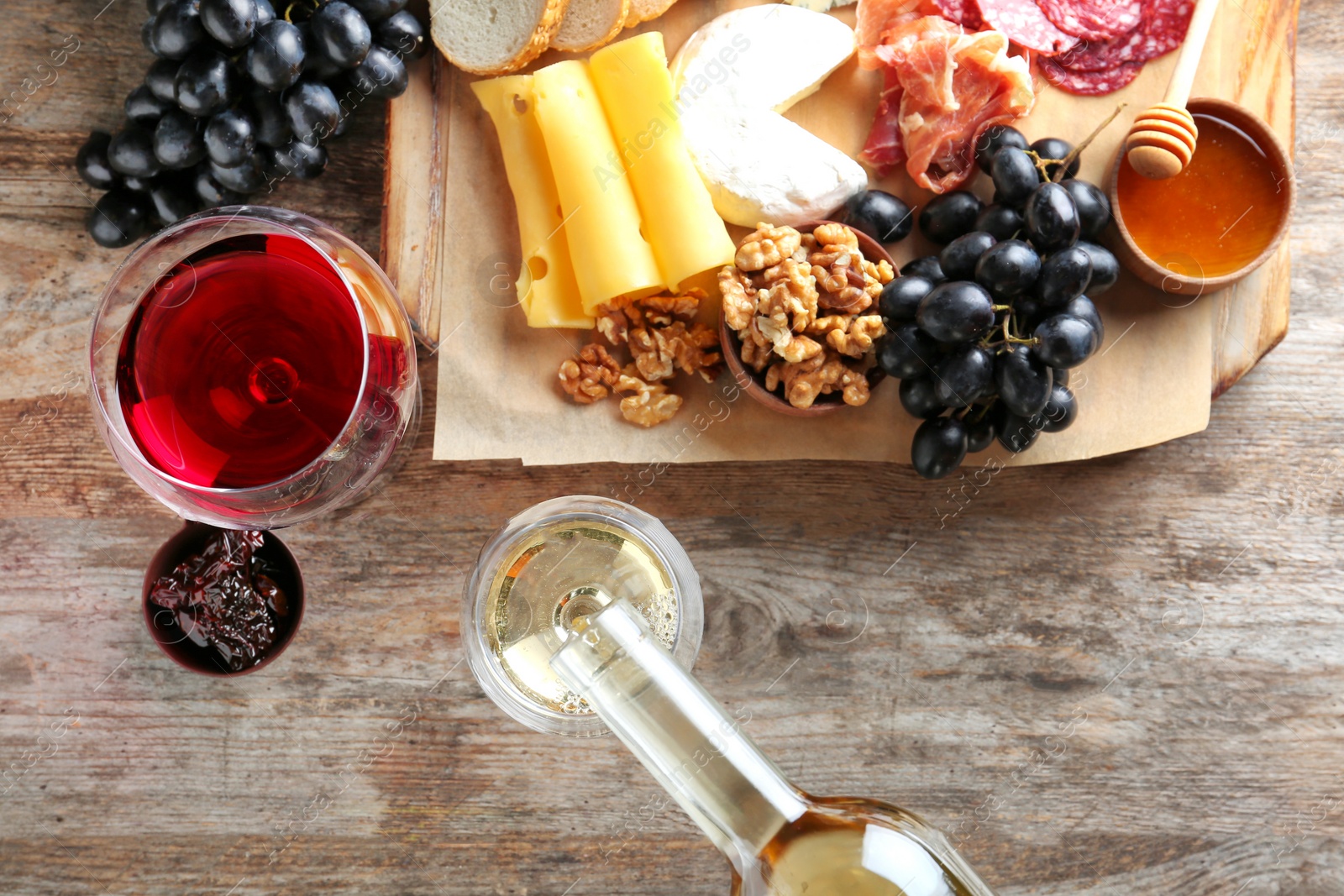 Photo of Pouring white wine into glass on table with delicious food, top view