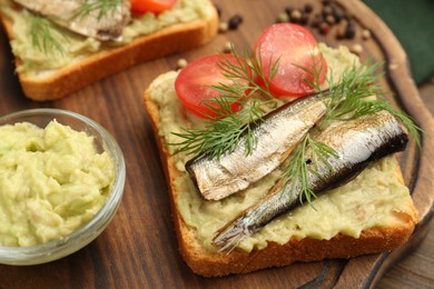 Photo of Delicious sandwich with sprats, tomato, dill and avocado puree on wooden board, closeup