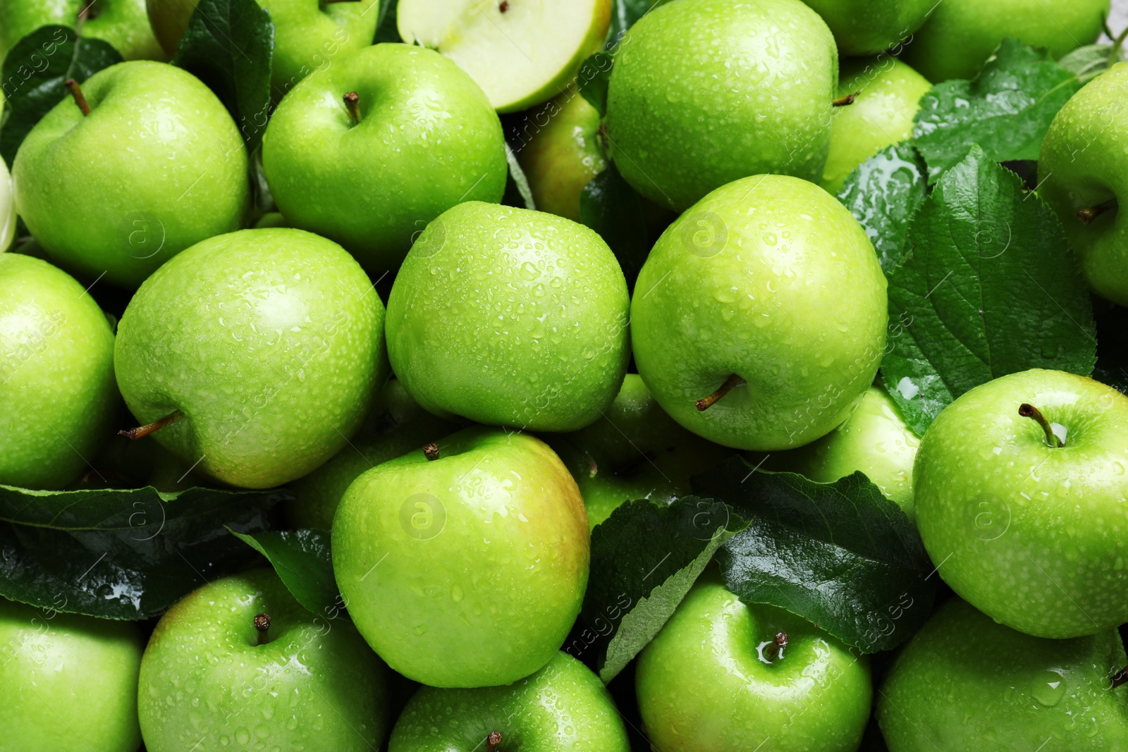 Photo of Pile of wet green apples with leaves as background, closeup