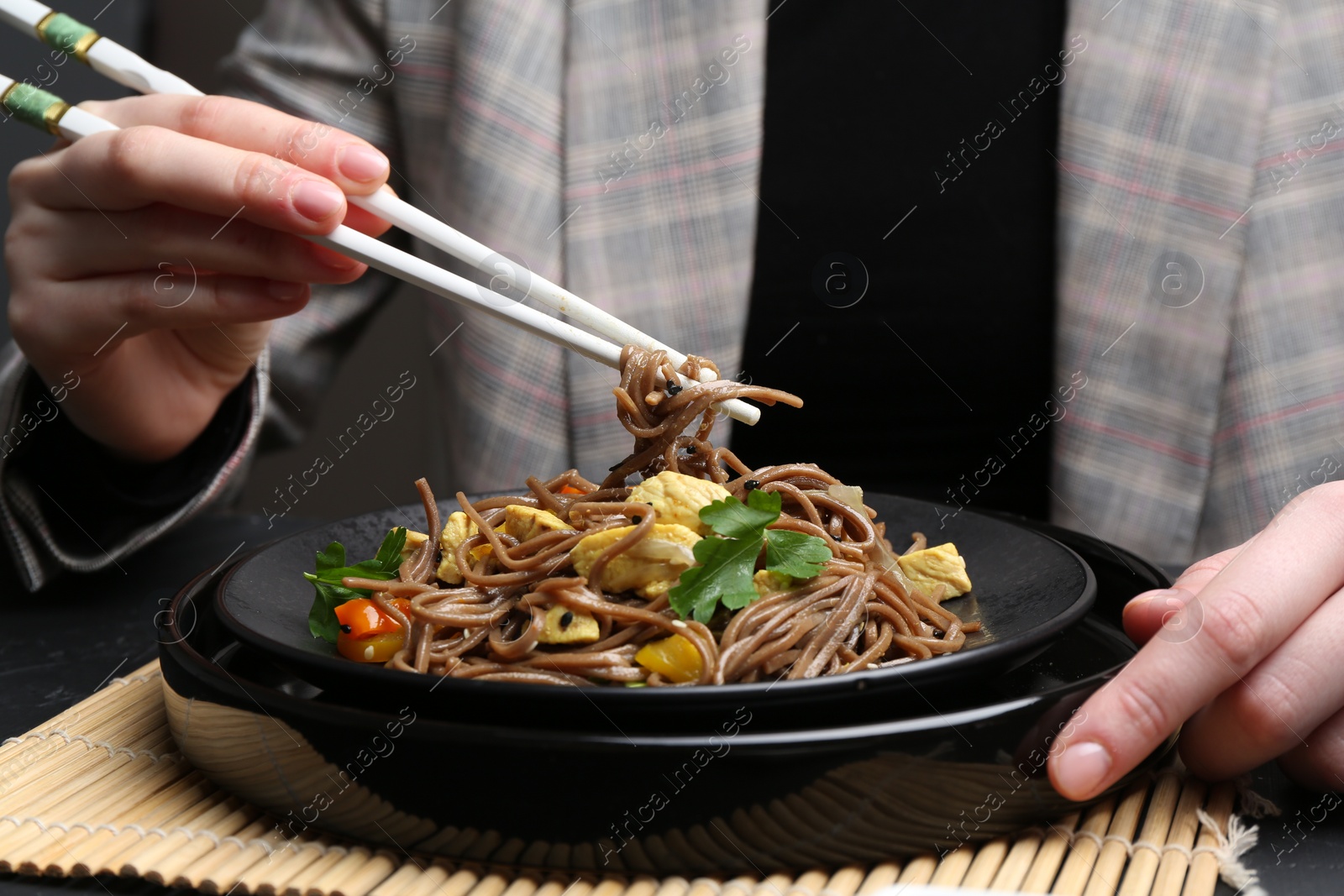 Photo of Stir-fry. Woman eating tasty noodles with meat and vegetables at dark table, closeup