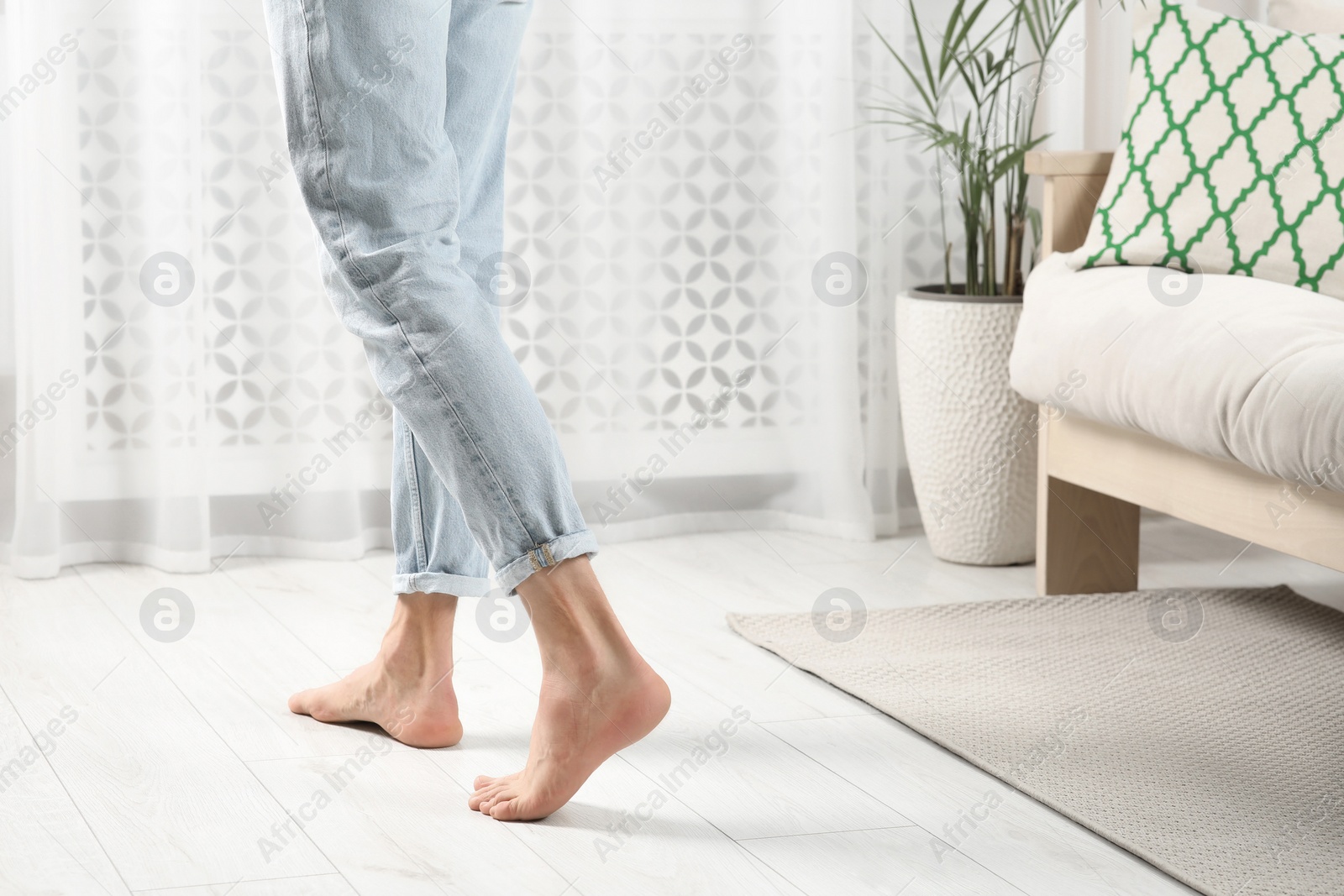 Photo of Barefoot woman walking on white parquet at home, closeup. Heated floor