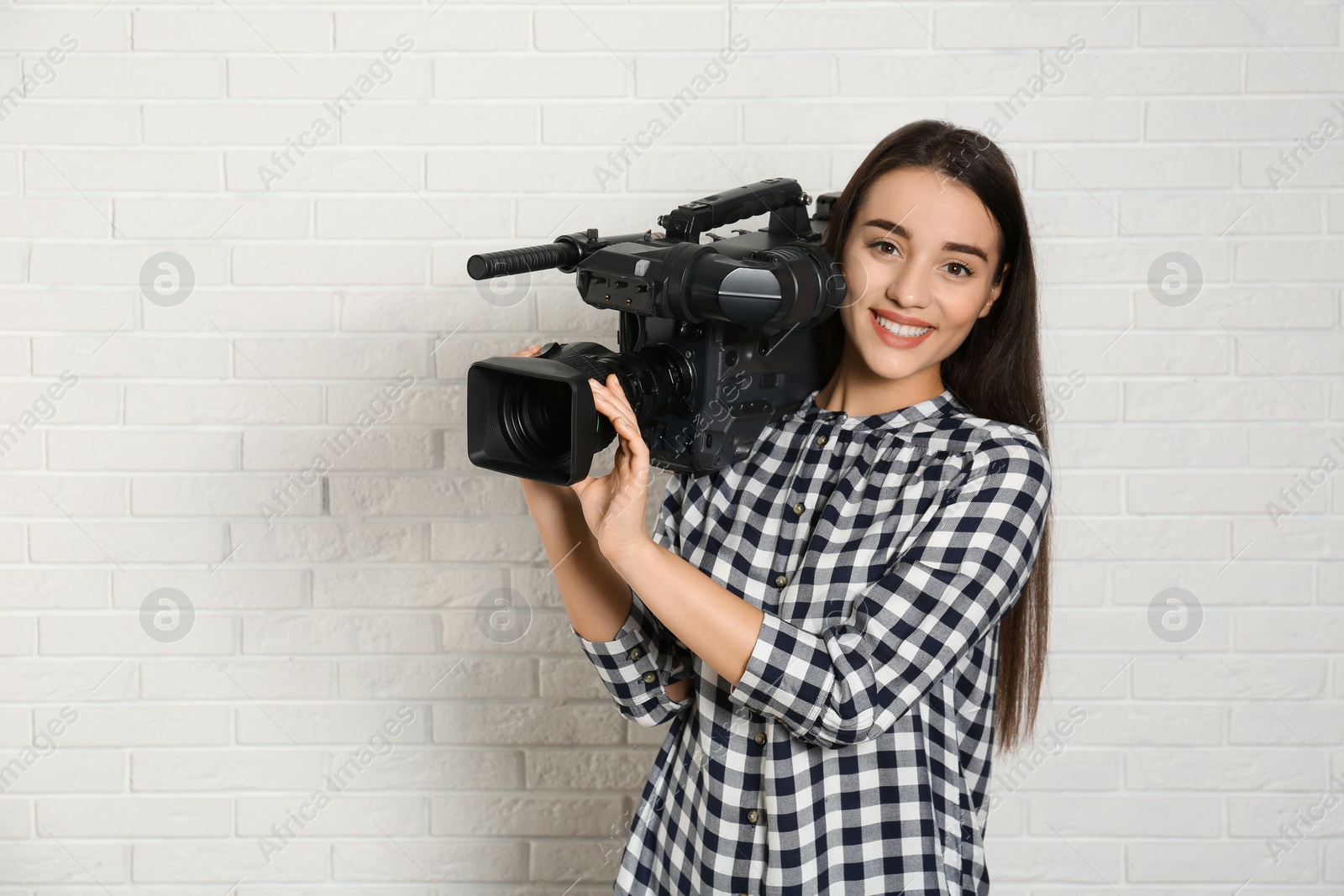 Photo of Operator with professional video camera near white brick wall