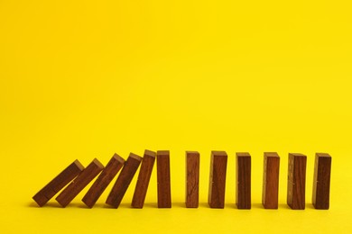 Photo of Falling wooden domino tiles on yellow background. Space for text