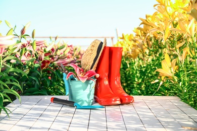 Gardening tools, rubber boots and fresh lily on white wooden table in flower field