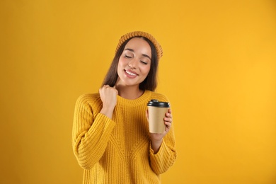 Happy beautiful woman with paper cup of mulled wine on yellow background