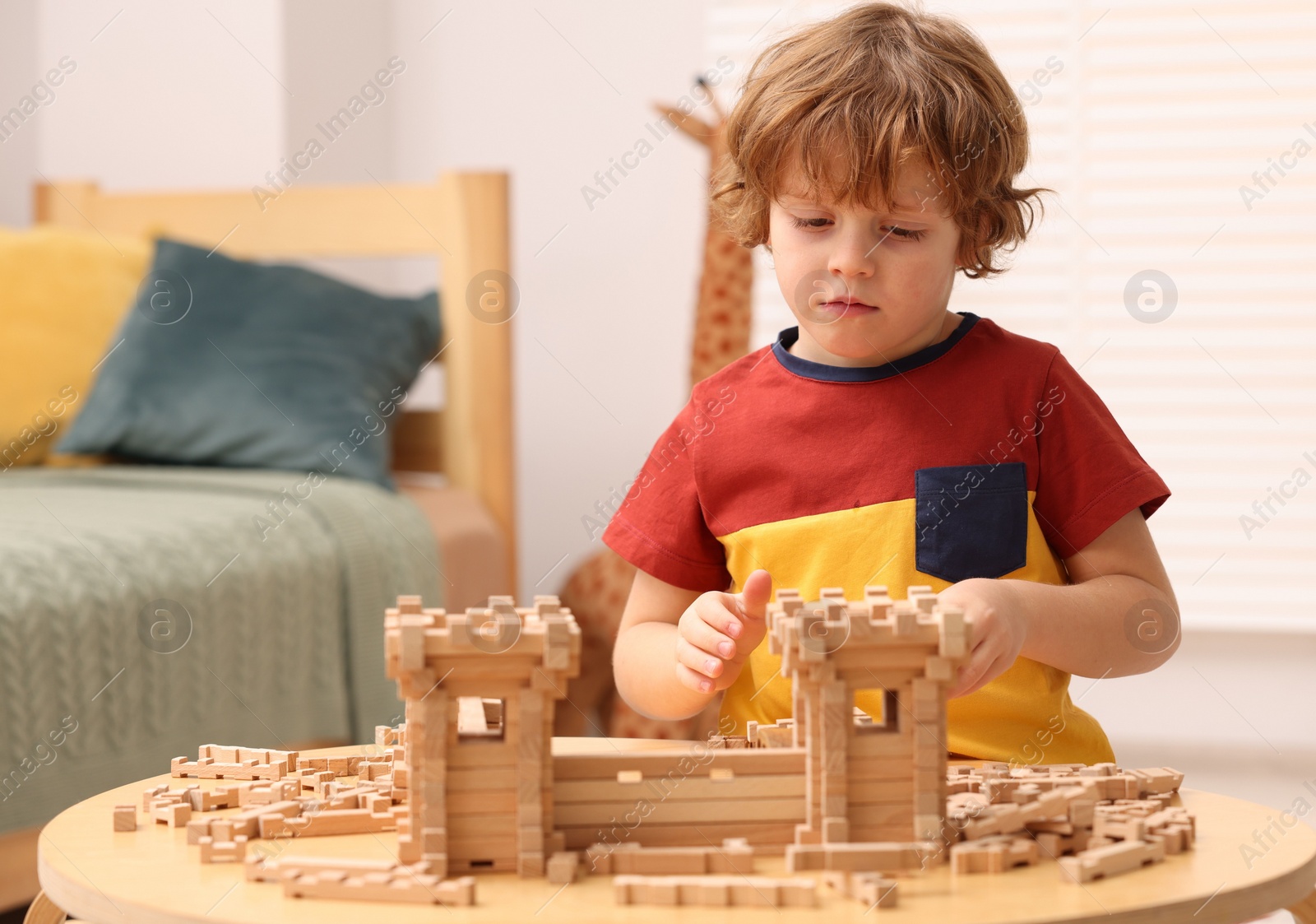 Photo of Cute little boy playing with wooden construction set at table in room. Child's toy