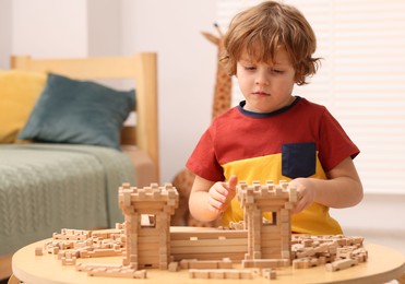 Cute little boy playing with wooden construction set at table in room. Child's toy