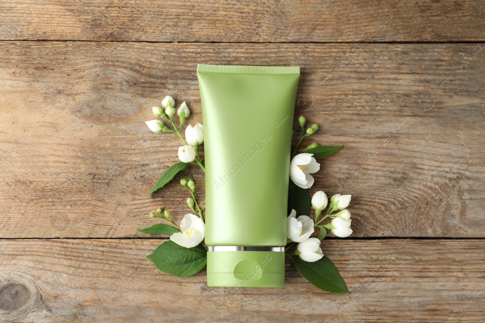 Photo of Tube of cosmetic product and flowers on wooden table, flat lay