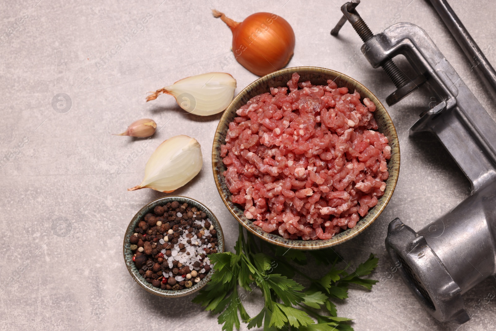 Photo of Manual meat grinder with beef mince, peppercorns, onion and parsley on light grey table, flat lay