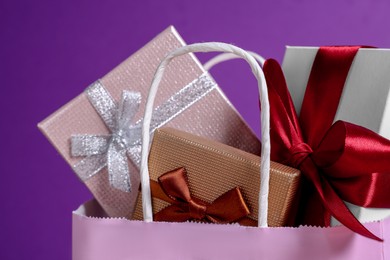 Photo of Pink paper shopping bag fullgift boxes on purple background, closeup