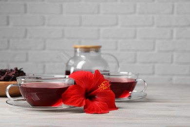 Photo of Delicious hibiscus tea and beautiful flower on light wooden table, space for text