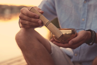 Photo of Man using Tibetan singing bowl outdoors, closeup