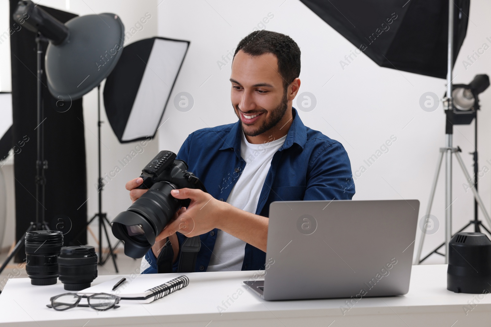 Photo of Young professional photographer with camera at table in modern photo studio