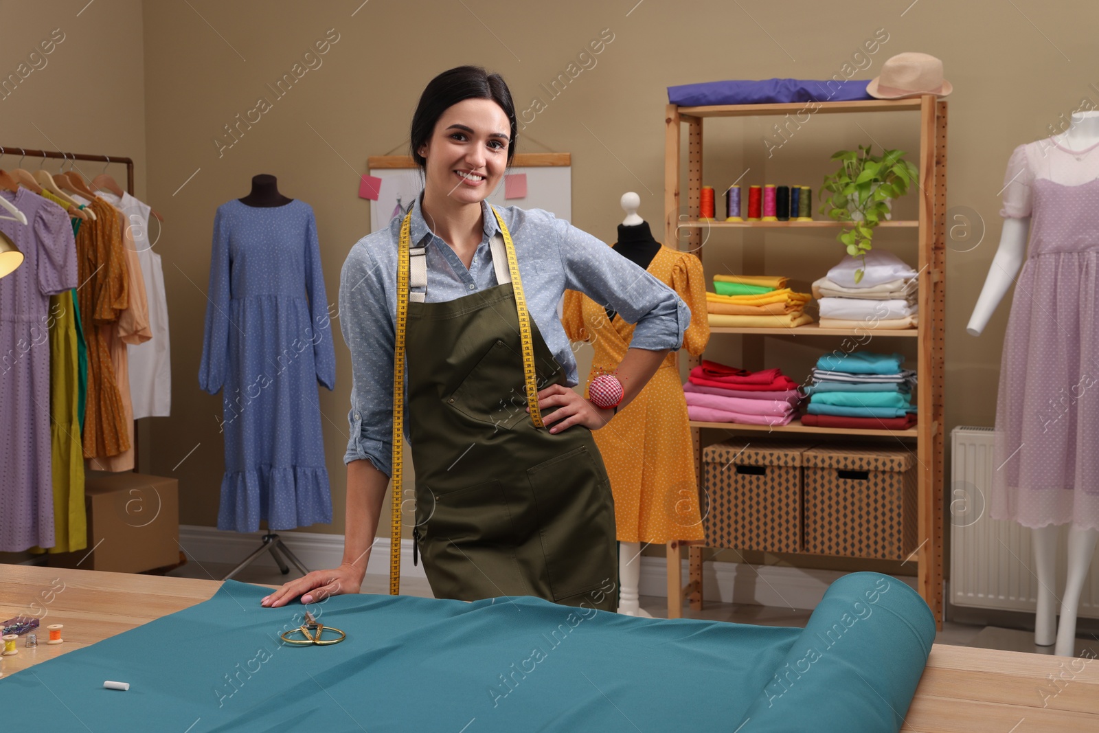 Photo of Dressmaker near table with light blue fabric in workshop