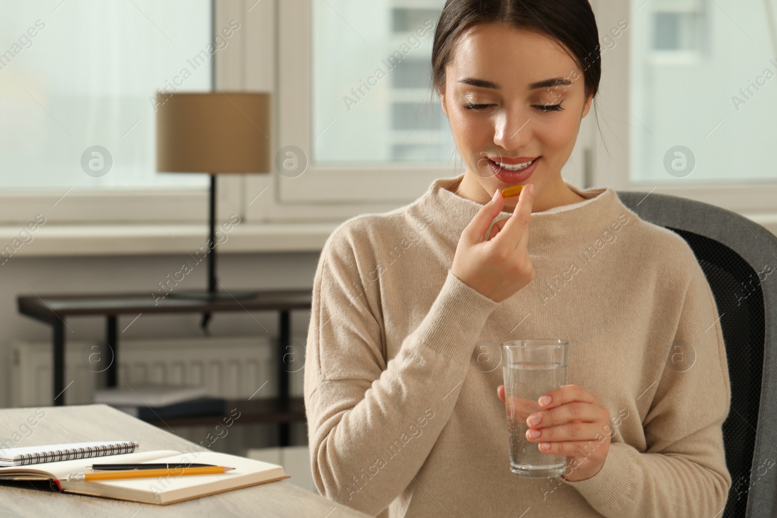 Photo of Young woman with glass of water taking dietary supplement pill indoors, space for text