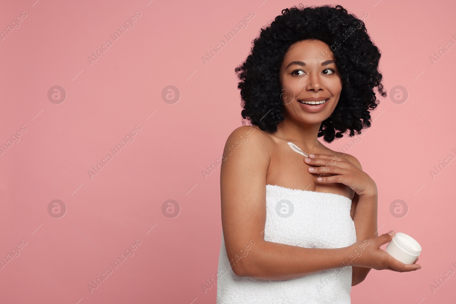 Photo of Young woman applying cream onto body on pink background. Space for text