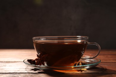 Photo of Glass cup of aromatic tea with anise stars on wooden table