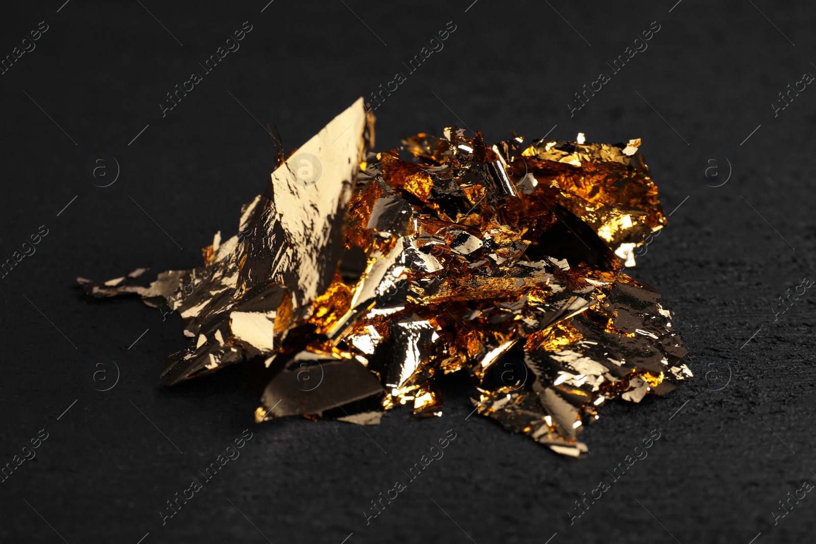 Photo of Pieces of edible gold leaf on black table, closeup