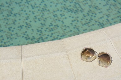 Stylish sunglasses near outdoor swimming pool on sunny day, space for text. Beach accessory