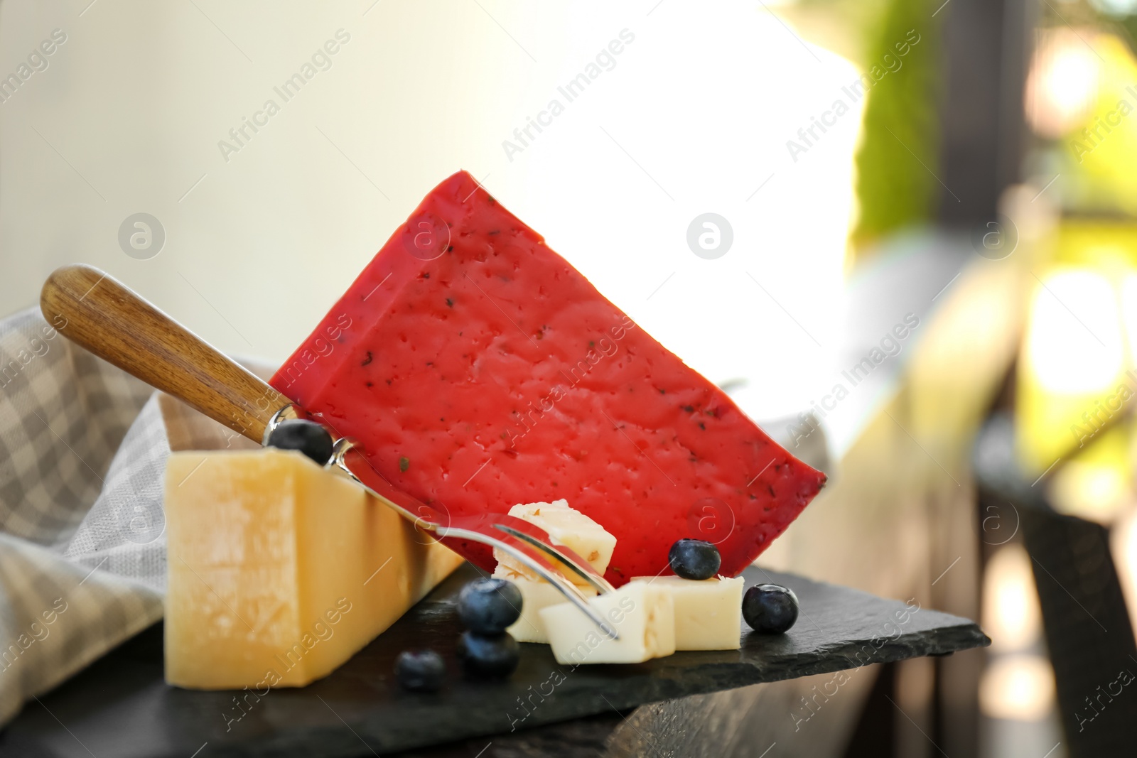 Photo of Different delicious cheeses, fork and blueberries on slate plate, closeup