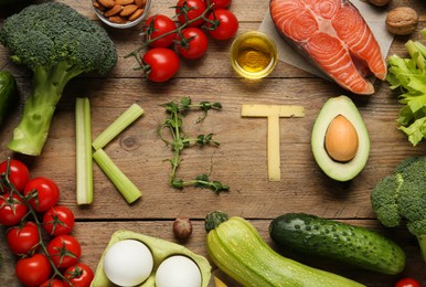 Word Keto made with products surrounded by different food on wooden table, flat lay