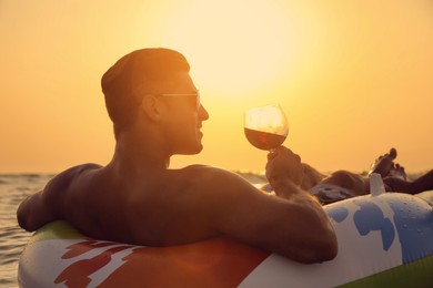 Photo of Man with glass of wine and inflatable ring in sea at sunset