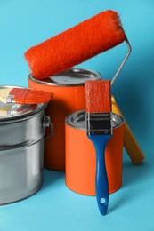 Photo of Cans of orange paint, bucket, roller and brushes on turquoise background