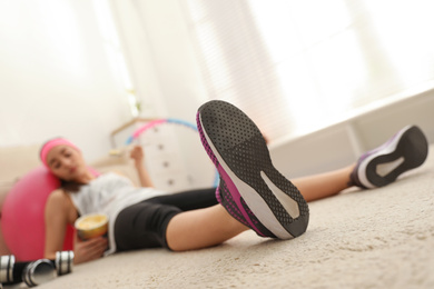 Photo of Lazy young woman eating ice cream instead of training at home, focus on legs