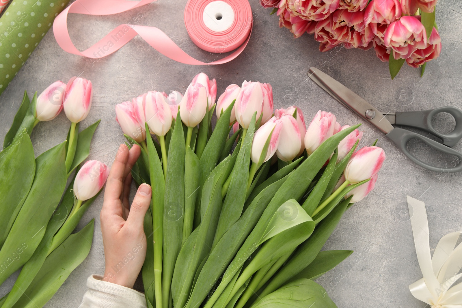 Photo of Woman making bouquet of beautiful fresh tulips at grey table, top view