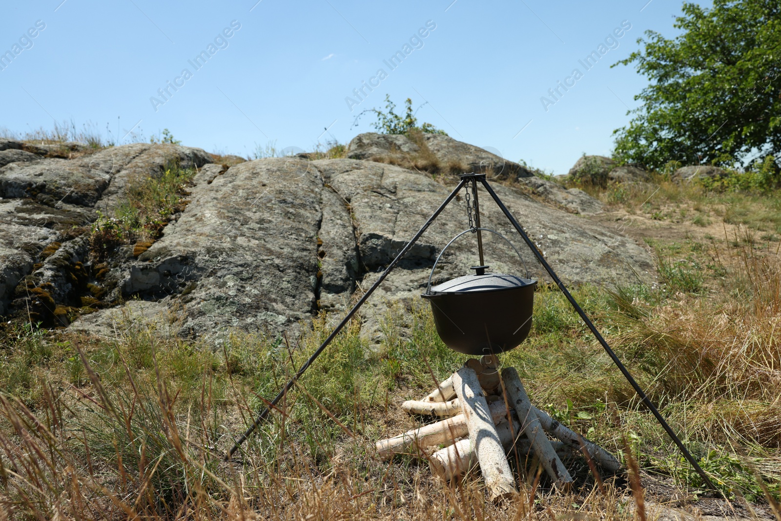 Photo of Cauldron above dry firewood arranged for bonfire outdoors. Camping season