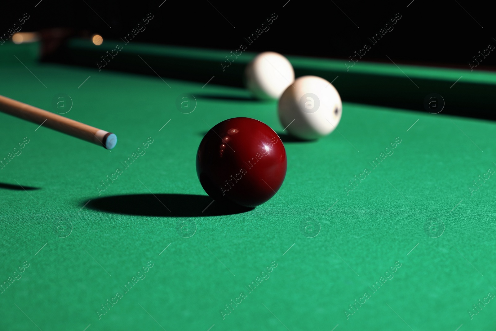 Photo of Striking red billiard ball with cue on table