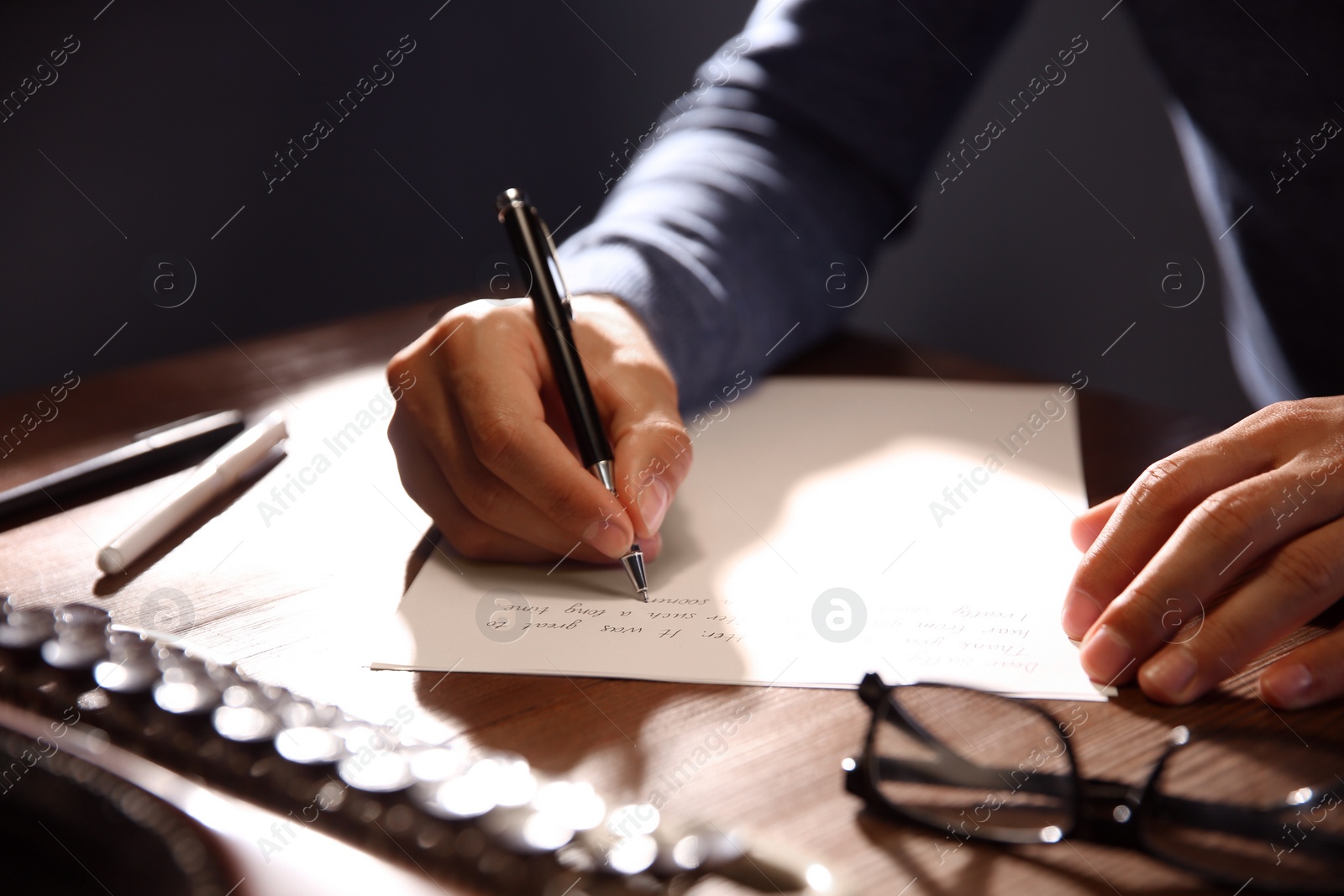 Photo of Man writing letter at wooden table indoors, closeup