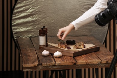 Photo of Food stylist creating beautiful composition with meat medallions on wooden table in photo studio, closeup