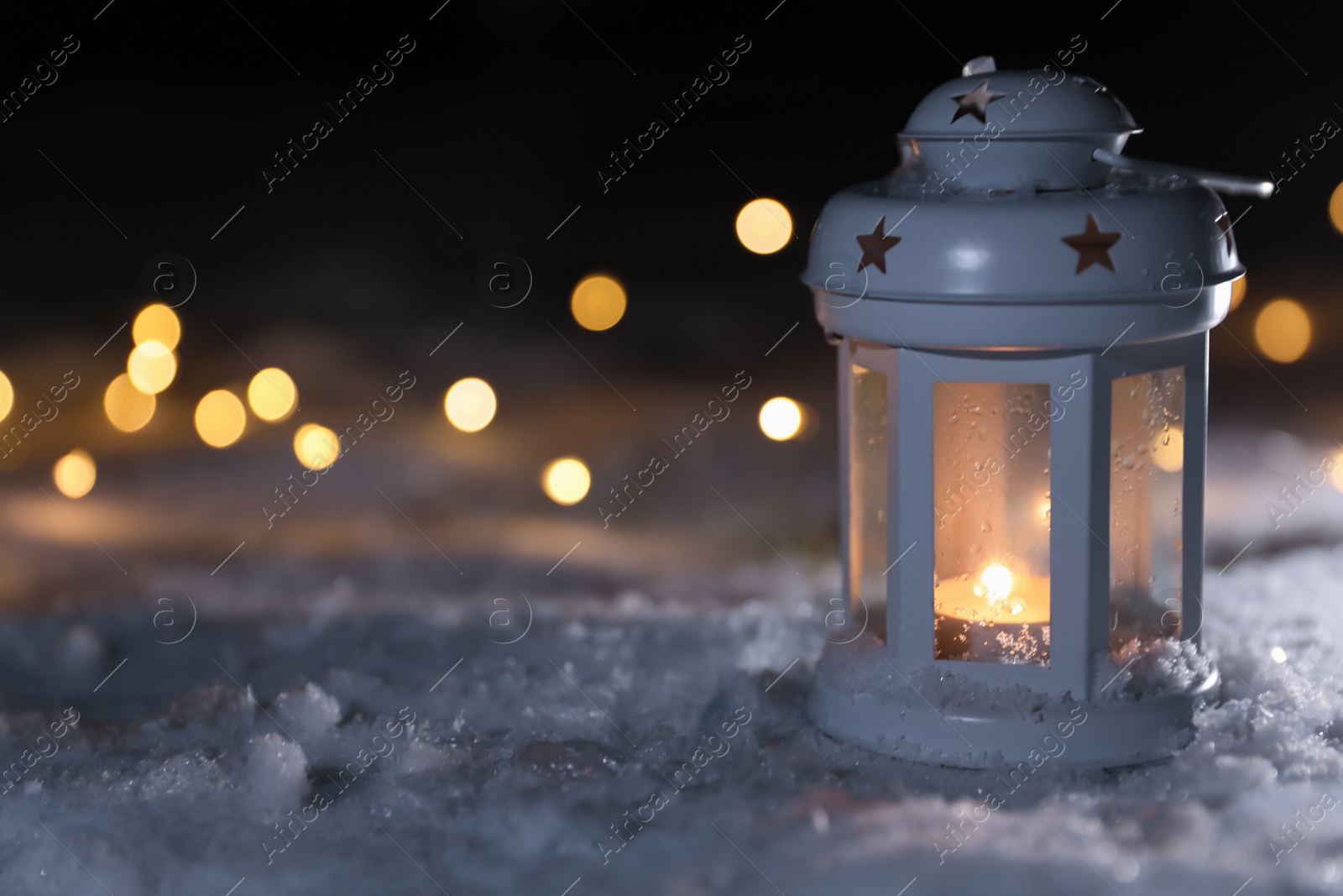 Photo of Lantern with burning candle and Christmas lights on white snow outdoors. Space for text