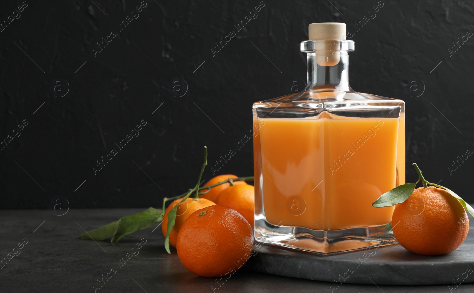 Photo of Delicious tangerine liqueur in glass bottle and fresh fruits on grey table, space for text