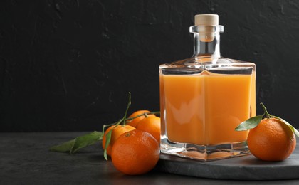 Photo of Delicious tangerine liqueur in glass bottle and fresh fruits on grey table, space for text